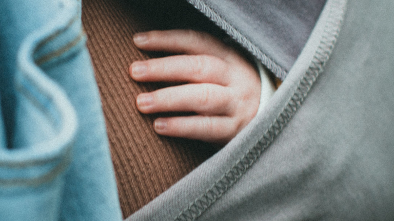 Baby hand peeking out of baby carrier on mom